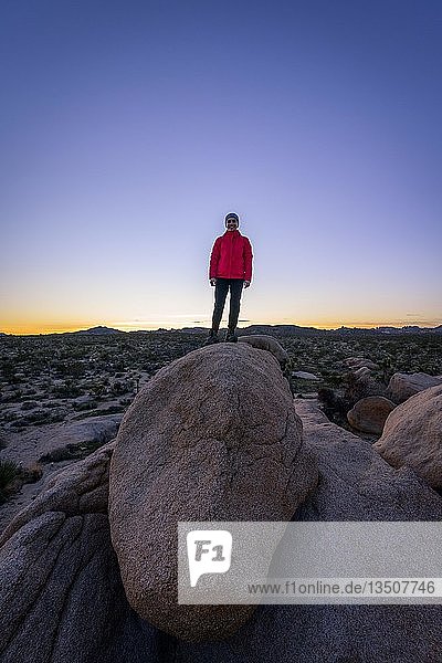 Junge Frau steht auf runden Granitfelsen bei Sonnenuntergang  Felsformationen  White Tank Campground  Joshua Tree National Park  Desert Center  Kalifornien  USA  Nordamerika