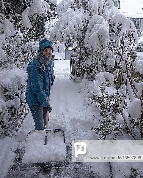Woman with a snow shovel clearing snow  Munich  Bavaria  Germany  Europe