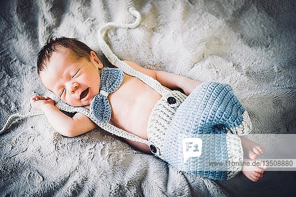 A newborn baby boy sleeping in blue and grey knitted bow tie and trousers  Portugal  Europe