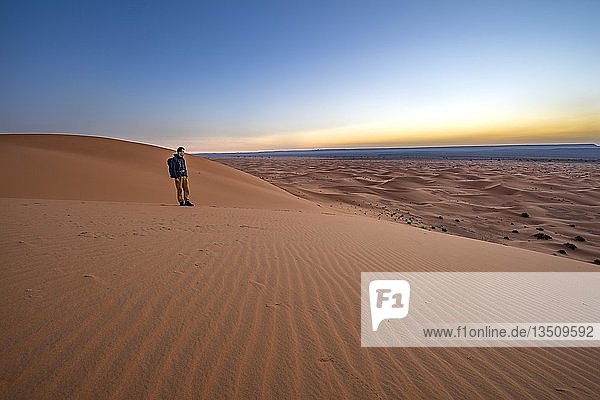 Junger Mann auf einer Sanddüne bei Sonnenaufgang  Erg Chebbi  Merzouga  Sahara  Marokko  Afrika