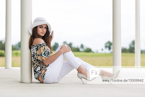 Young woman sitting with white pants and hat