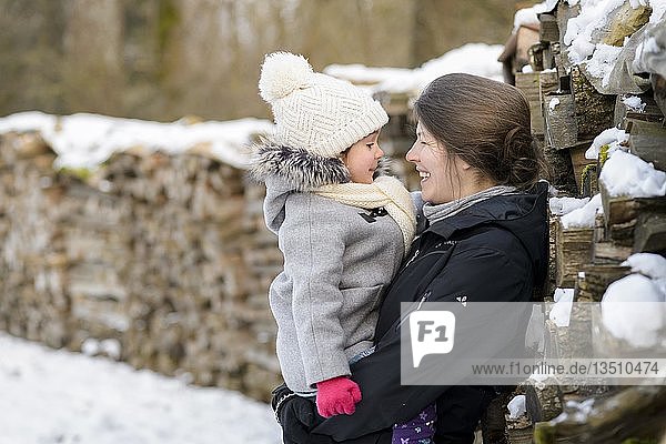 Mother  35 years with girl  4 years  on her arm  standing next to stacked wood in winter  Baden-Württemberg  Germany  Europe