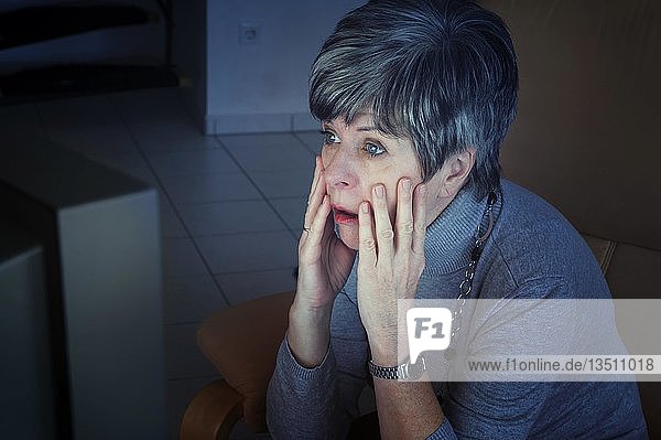 Frau  die vor ihrem Fernseher sitzt und schockiert die Nachrichten verfolgt