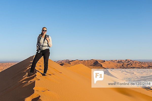 Frau steht auf einer roten Sanddüne in der Wüste  Dünenlandschaft Erg Chebbi  Merzouga  Sahara  Marokko  Afrika