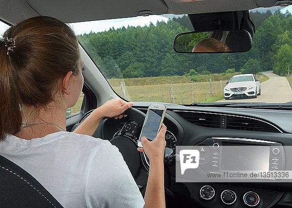 Junge Frau  die ein Mobiltelefon benutzt  während sie ein Auto fährt  Schweden  Europa