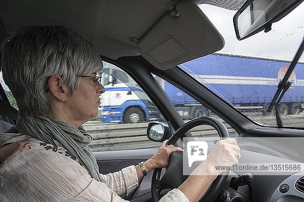 Woman sitting behind the steering wheel of a car  she is driving on the motorway  Lower Saxony  Germany  Europe