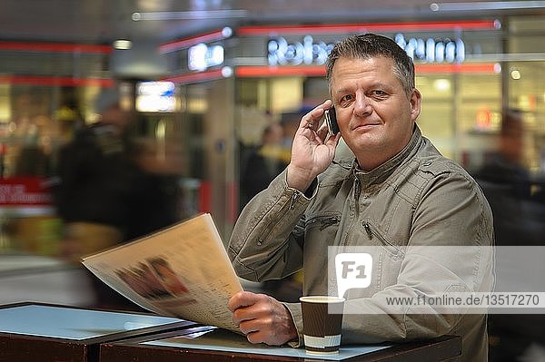 Mann mit einer Zeitung und einem Mobiltelefon in einem Einkaufszentrum  Düsseldorf  Nordrhein-Westfalen  Deutschland  Europa