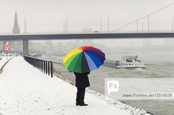 Frau steht mit einem bunten Regenschirm im Winter am Rheinufer  Düsseldorf  Rheinland  Nordrhein-Westfalen  Deutschland  Europa