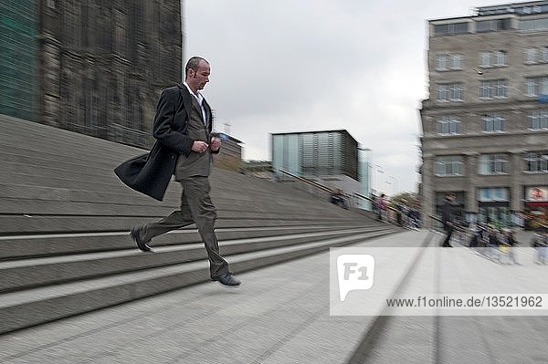 Junger Mann in schwarzem Mantel springt eine Treppe hinunter
