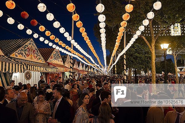 Spanier feiern in traditioneller Kleidung vor beleuchteten Festzelten  Casetas am Abend  geschmückte Straße  Feria de Abril  Sevilla  Andalusien  Spanien  Europa