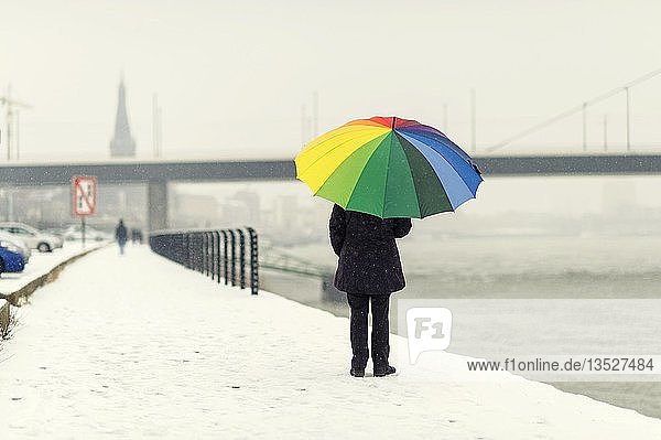 Frau steht mit einem bunten Regenschirm im Winter am Rheinufer  Düsseldorf  Rheinland  Nordrhein-Westfalen  Deutschland  Europa