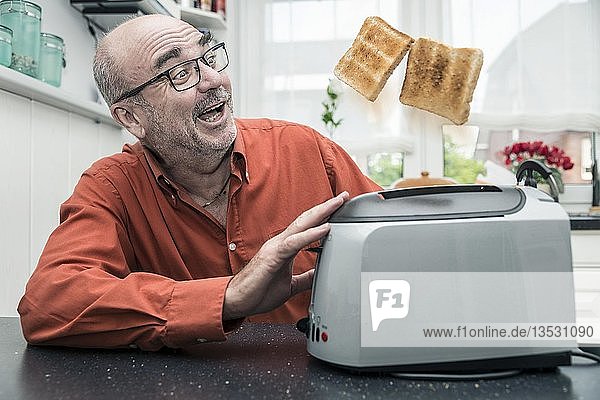 Mann beobachtet  wie 2 Scheiben Toast aus einem Toaster ausgeworfen werden  Deutschland  Europa