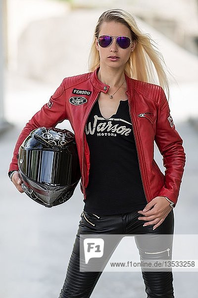 Young woman with long blonde hair poses posing with motorcycle helmet and sunglasses