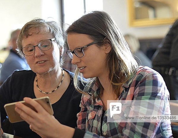 Junge und ältere Frau schauen auf Smartphone  Portrait  Café  Stuttgart  Baden-Württemberg  Deutschland  Europa