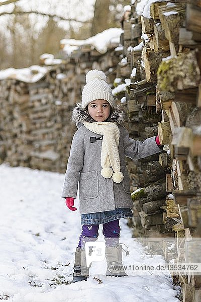 Mädchen  4 Jahre alt  mit Mantel im Winter neben gestapeltem Holz  Baden-Württemberg  Deutschland  Europa