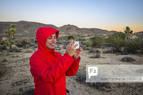 Young woman photographs with her smartphone in the desert  White Tank Campground  Joshua Tree National Park  Desert Center  California  USA  North America