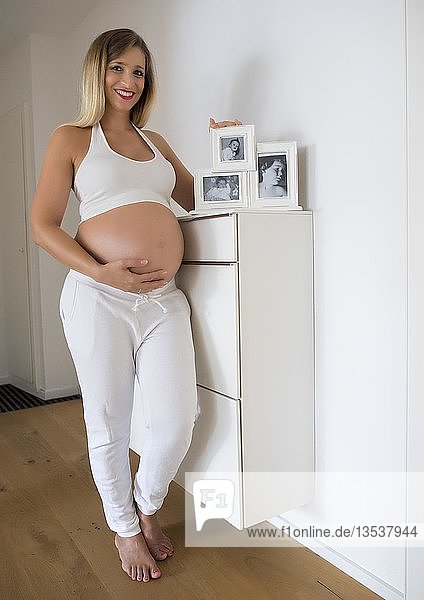 Frau im neunten Monat schwanger  posiert vor Babyfotos mehrerer Generationen  Deutschland  Europa