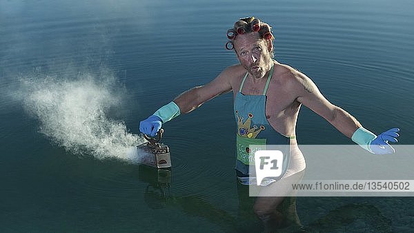 Man with curlers in his hair looking in the water  ironing the water surface with steam iron  Germany  Europe