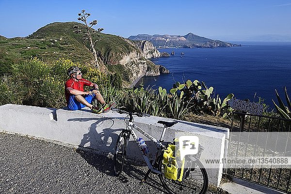 Cyclist pausing on the Belvedere Quattrocchi with a view over the rocks Faraglione on the island Vulcano  Pianoconti  Lipari  Aeolian Islands  Sicily  Italy  Europe