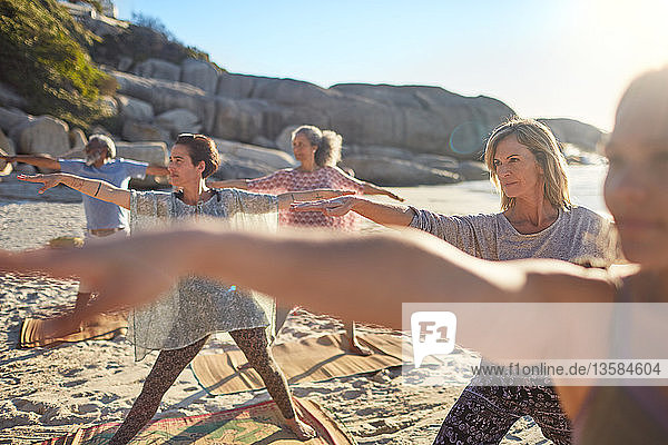 Group practicing yoga on sunny beach during yoga retreat