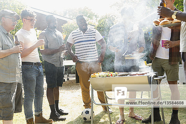 Männliche Freunde trinken Bier und grillen im sonnigen Sommergarten