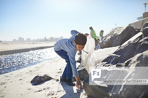 Boy volunteer picking up litter on sunny beach