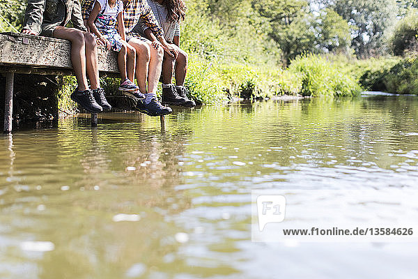 Familie mit baumelnden Füßen auf dem sonnigen Steg am Flussufer