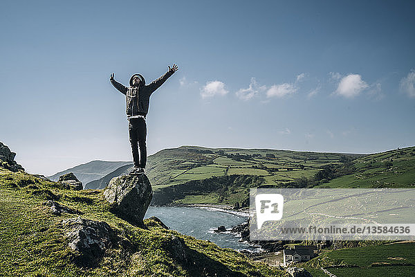Unbekümmerter Mann auf einem Felsen stehend mit Blick auf eine sonnige  idyllische Landschaft  Nordirland