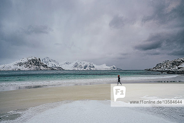 Frau,  die am kalten,  verschneiten Strand spazieren geht,  Lofoten-Inseln,  Norwegen