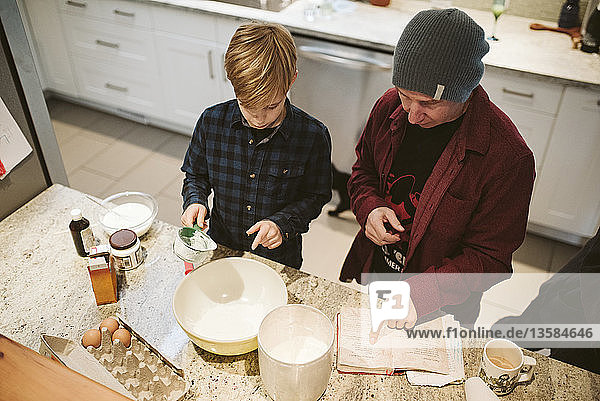 Vater und Sohn beim Backen  mit Blick auf das Rezept in der Küche