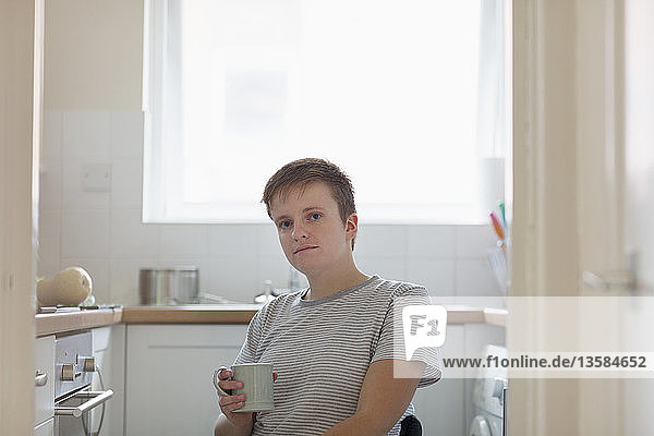Porträt einer selbstbewussten jungen Frau im Rollstuhl  die in einer Wohnküche Kaffee trinkt