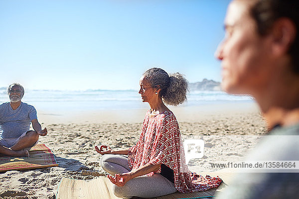 Gelassene ältere Frau meditiert am sonnigen Strand während eines Yoga-Retreats