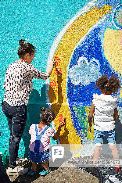 Mutter und Tochter malen als Freiwillige ein lebendiges Wandgemälde an eine sonnige Wand
