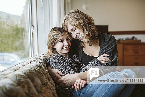 Affectionate mother and daughter cuddling on living room sofa