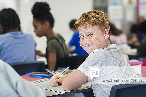 Portrait smiling  confident junior high school boy student studying at desk in classroom