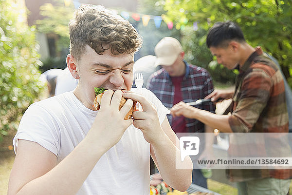 Hungriger Teenager isst Hamburger beim Grillen im Hinterhof