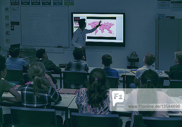 Schüler beobachten den Geografielehrer auf der Projektionsfläche im dunklen Klassenzimmer