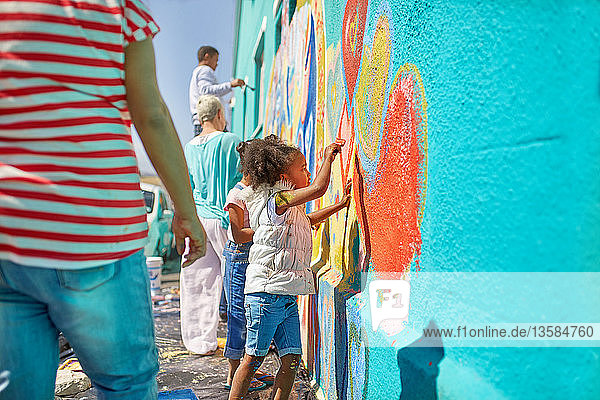 Girl volunteer painting vibrant mural on sunny wall