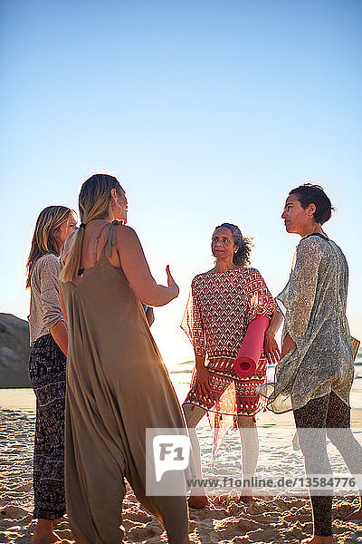 Women with yoga mats talking on sunny beach during yoga retreat