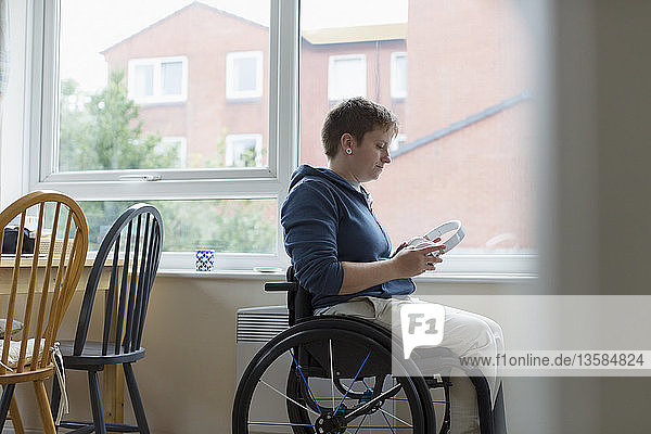 Junge Frau im Rollstuhl mit Kopfhörern am Fenster