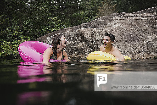 Glückliches junges Paar schwimmt in aufblasbaren Ringen auf dem See