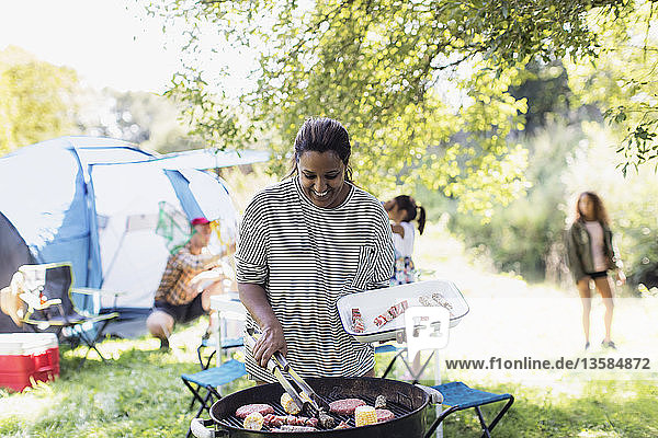 Lächelnde Frau beim Grillen des Mittagessens für die Familie auf dem Campingplatz