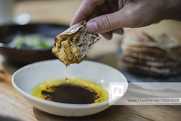 Close up hand dipping bread in olive oil and balsamic vinegar