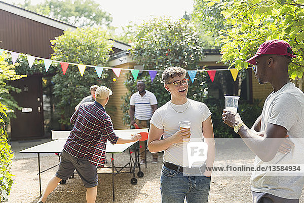 Männliche Freunde trinken Bier und spielen Tischtennis im Sommer Hinterhof