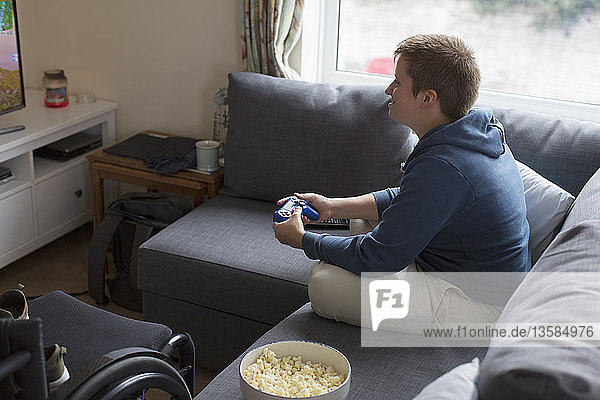 Junge Frau spielt ein Videospiel auf dem Sofa neben dem Rollstuhl