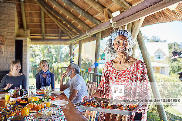 Portrait smiling senior woman serving food to guests in hut