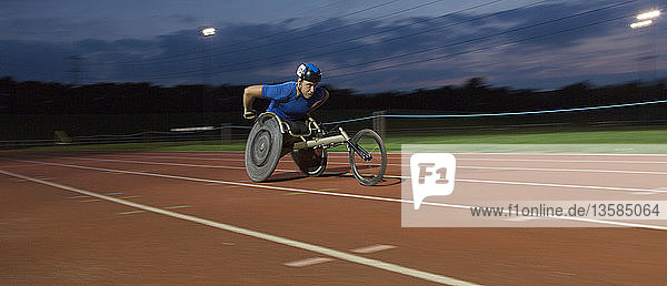 Determined young male paraplegic athlete speeding along sports track in wheelchair race at night
