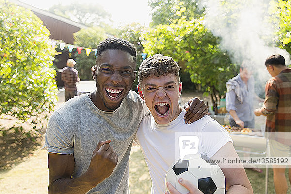Porträt begeisterter junger Männer mit Fußball  die jubelnd im Hinterhof grillen