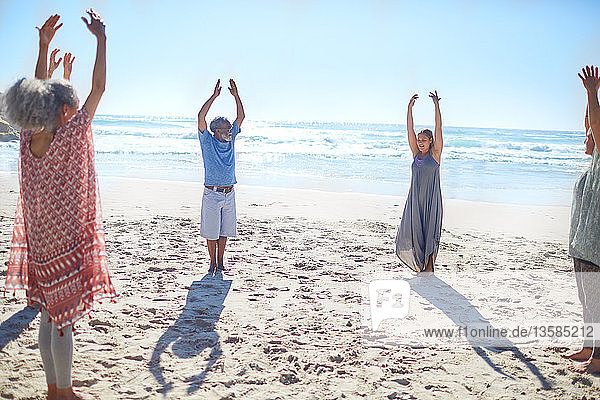 Gruppe steht mit erhobenen Armen im Kreis am sonnigen Strand während eines Yoga-Retreats