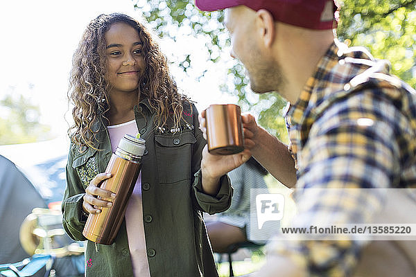 Tochter schenkt ihrem Vater auf dem Campingplatz Kaffee aus einem isolierten Getränkebehälter ein